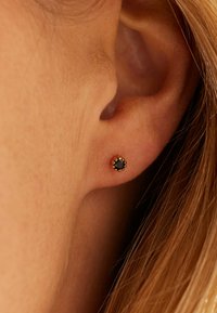 Zwarte edelsteen studoorbel met een ronde vorm, gezet in roségoudkleurig metaal, met een getextureerde bezel voor extra detail.