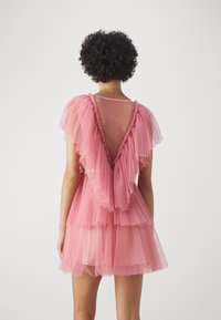 Robe en tulle rose avec des volants superposés, dos en V profond et manches courtes. Texture douce, tissu léger et silhouette évasée.