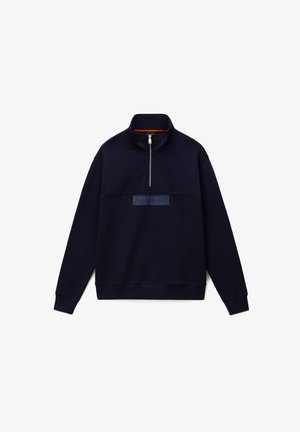 Sudadera polar azul marino con cuello alto, cremallera frontal hasta la mitad y un parche de logo texturizado en el pecho. Puños y bajo acanalados para un ajuste ceñido.