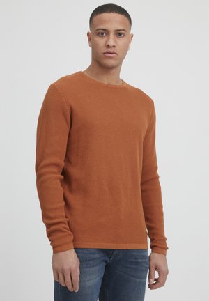 Pullover din bumbac de culoare portocalie arsă, cu mâneci lungi și un guler rotund, stilizat cu blugi, purtat pe un fundal neutru.