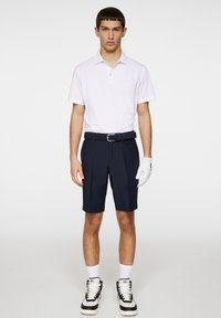 Vit polo skjorta, marinblå shorts och vit golfhandske. Svart- och vit sportskor. Avslappnad design, korta ärmar och ett strukturerat bälte.