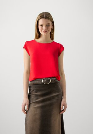 Red short-sleeve top with a rounded neckline, worn with a brown denim skirt featuring a large silver circular belt buckle. Smooth texture.