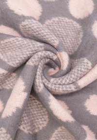 Coperta grigia con grandi pois rosa, caratterizzata da una consistenza morbida e pelosa. Il tessuto ha una leggera lucentezza, che ne sottolinea l'aspetto accogliente.