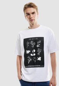 Camiseta blanca de algodón con gráficos florales en arte lineal en la parte frontal, con el texto "LINE ART FLORA" en la parte superior y detalles debajo.