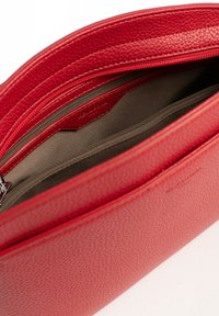 Pocchetto in pelle rossa con finitura testurizzata, dotato di chiusura con zip e scomparti interni foderati in tessuto scuro. Nessun accento decorativo visibile.