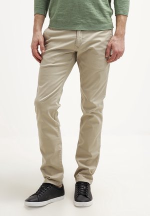 Beige chinos with a slim fit, made from cotton. Paired with black sneakers featuring a textured design and white rubber soles.