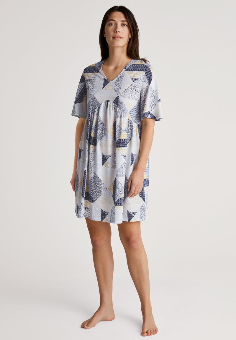 Patchwork jurk in lichtblauw, met verschillende geometrische patronen in marineblauw, geel en wit. Korte mouwen en een V-hals ontwerp.