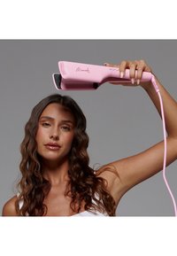 Plancha plana en rosa pastel con un acabado suave, diseñada con una forma redondeada y un agarre texturizado, que cuenta con un cable de alimentación.