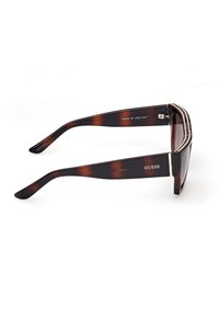 Lunettes de soleil rectangulaires écaille de tortue avec détail en strass sur la partie supérieure de la monture et logo "GUESS" sur la branche.