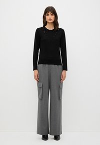 Maglietta nera a maniche lunghe con scollo a V e dettagli a cut-out, abbinata a pantaloni grigi a righe con gamba larga e tasche cargo. Stivaletti neri.