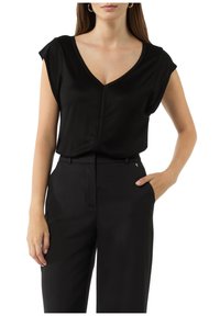 Schwarzes, eng anliegendes Oberteil mit kurzen Ärmeln, V-Ausschnitt und glatter Textur; kombiniert mit hoch taillierten schwarzen Hosen mit Seiten Taschen.