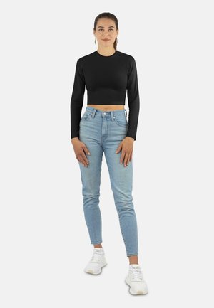 Schwarz langärmliges cropped Top, hellblaue high-waisted Jeans und weiße Sneakers. Das Outfit zeichnet sich durch ein figurbetontes Design mit einer glatten Textur aus.
