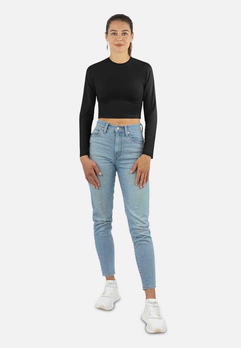 Schwarz langärmliges cropped Top, hellblaue high-waisted Jeans und weiße Sneakers. Das Outfit zeichnet sich durch ein figurbetontes Design mit einer glatten Textur aus.