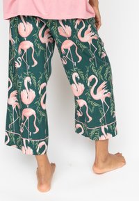 Blumige Pyjamahosen in Dunkelgrün, mit einem Muster aus rosa Flamingos und blättrigen Akzenten. Lockere Passform, cropped Länge, weicher Baumwollstoff.