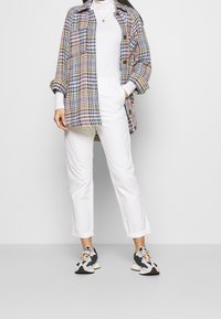Camisa de cuadros multicolor en tejido de punto, cuello alto blanco, pantalones cortos blancos y zapatillas azul y crema. Corte relajado.