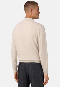 Hellbeige Strickpoloshirt mit langen Ärmeln, gerippten Bündchen und flachem Kragen. Glatte Textur, taillierte Passform und keine sichtbaren Muster.