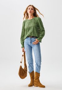 Groen kanten top met lange mouwen met bloemenpatronen, lichtblauwe strakke jeans, bruine suède slappe laarzen en een bruine schoudertas met een brede riem.