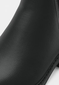 Sorte skinn ankelstøvler med glatt tekstur, rund form og minimale sømmer. Har en lav hæl og et rent, enkelt design.