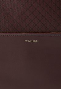 Bordeaux portemonnee met een textuurmateriaal met een herhalend patroon, gouden "Calvin Klein" logo en contrasterende stiksel details.