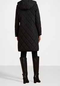 Svart quiltad parkas med huva, med ett diamantmönster. Bärs över svarta leggings och knähöga läderstövlar med klack.