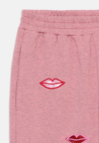 Fato de treino rosa com lábios bordados em vermelho e detalhes brilhantes. Cintura elástica com um acabamento de tecido suave e texturizado.