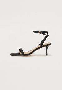 Sandale noire à talon carré, avec une fine bride au niveau de la cheville et un talon brillant de 6 cm. Matériau lisse avec une finition mate.