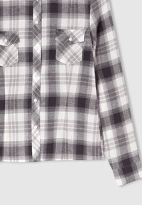Camicia in flanella a quadri grigi e bianchi con maniche lunghe, due taschini sul petto e chiusura con bottoni. Presenta un motivo a scacchi con una texture morbida.