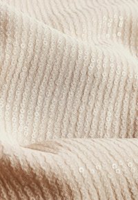 Woven fabric u mekom bež tonu s teksturiranim, valovitim uzorkom i raspršenim sjajnim šljokicama kao naglasak. Glatka i blago reflektirajuća površina.