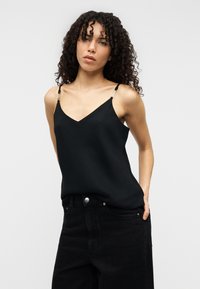 Μαύρο σατέν καμησόλ με V-λαιμόκοψη, λεπτές τιράντες με ασημί διακοσμητικά, συνδυασμένο με ψηλόμεσα μαύρα τζιν παντελόνια.