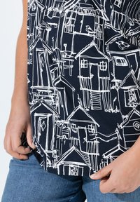 Camisa negra con un patrón de casas dibujado en blanco. Mangas cortas y tela ligera con un corte relajado. Combinada con denim.