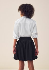 Witte blouse met opgerolde mouwen, gecombineerd met een zwarte, knie-lange, uitlopende rok met een elastische tailleband.