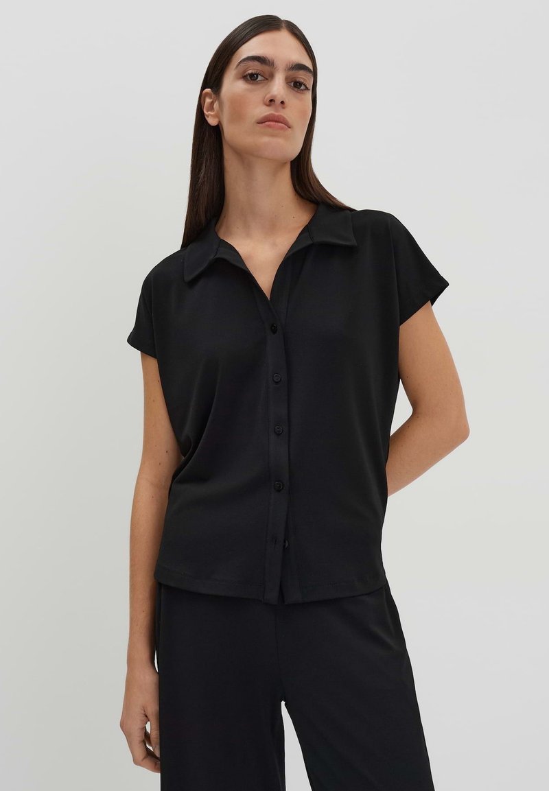 Zwarte korte mouwen blouse met een kraag, gemaakt van een gladde stof. Heeft een ontspannen pasvorm en een subtiele glans. Gecombineerd met bijpassende broek.