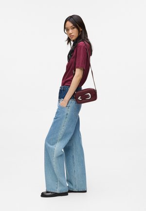 Mörkröd t-shirt, ljusblå vida jeans, svart scarf och en röd crossbody-väska med silverdetaljer. Slätt tyg och avslappnad passform.