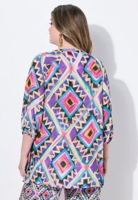 Mehrfarbige Tunika mit einem geometrischen Muster aus Diamanten in Lila, Rosa, Orange und Blau. Lockere Passform mit 3/4-Ärmeln.