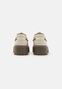 Sapatos de cor creme com detalhes em castanho, sola plataforma grossa e duas tiras atrás para um ajuste seguro. Detalhes texturizados na parte superior.