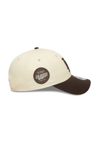 Gorra de béisbol con la parte superior de color beige claro y visera marrón. Presenta un parche redondo con el logo en el lateral que dice "Los Angeles Dodgers" en blanco.
