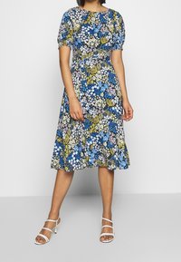 Kwiatowa sukienka z dopasowaną talią, krótkimi bufkami i długością do kolan. Ozdobiona niebieskimi, żółtymi i białymi wzorami na czarnym tle.