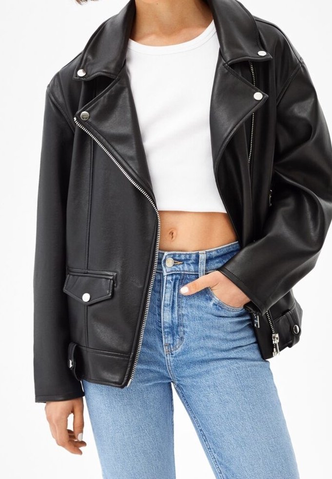 Giubbotto da biker in ecopelle nera con colletto a punte, dettagli in argento, tasche laterali e vestibilità rilassata, abbinato a jeans blu a vita alta.