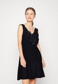 Vestuário preto com um decote em V profundo e bordados florais na gola. Apresenta uma cintura ajustada com um cinto. Feito de tecido suave.