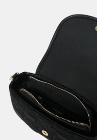 Borsa a tracolla in pelle nera trapuntata con chiusura a scatto dorata, aperta per rivelare un compartimento principale e una tasca zip interna più piccola.
