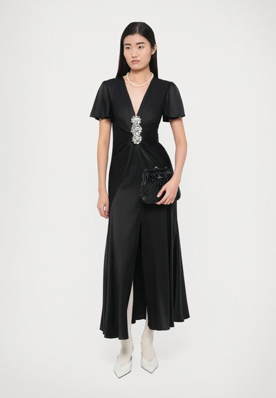 Fekete szatén estélyi ruha rövid, lebbenő ujjakkal, V-nyakkivágással, ékszeres derékrésszel és bő szoknyával. Fekete kuplung táskával kiegészítve.