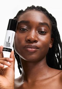Hydrating serum in a white and black cylindrical bottle, held by a person with textured hair. Skin appears smooth and glowing.