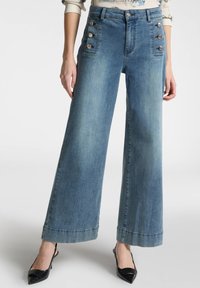 Pantaloni in denim a vita alta e gamba larga di colore azzurro, con bottoni decorativi ai lati, cuciture a contrasto e orlo dritto.