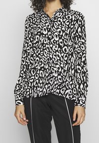 Bluse med sort-hvid leopardprint, knap-opsat krave, lange ærmer, afslappet pasform og en glat stofstruktur.