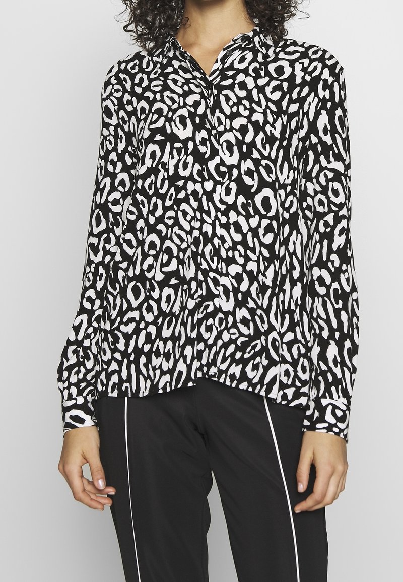 Bluse med sort-hvid leopardprint, knap-opsat krave, lange ærmer, afslappet pasform og en glat stofstruktur.