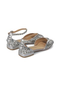 Bailarinas metálicas plateadas con un diseño abierto, adornadas con tachuelas plateadas y correas, con un bajo tacón cuadrado y un interior de cuero suave.