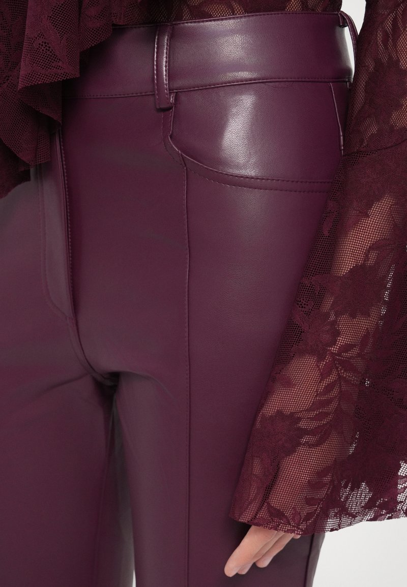 Bordeaux faux leren broek met een gladde textuur en een nauwsluitend ontwerp, gecombineerd met een doorschijnende kanten top met bloemenpatronen en wijde mouwen.
