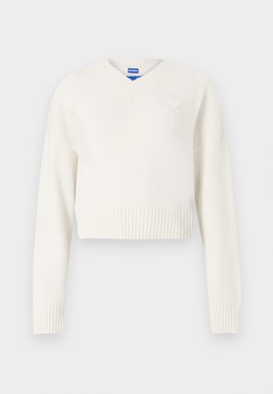 Pull court blanc en maille douce. Présente un col en V, un ourlet côtelé et un petit emblème en forme de cœur sur la poitrine gauche.