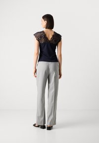 Haut marine avec détail en dentelle dans le dos, manches courtes ; associé à un pantalon large gris clair ; tissu lisse et fines rayures verticales.
