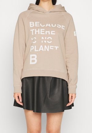 Beige hoodie met witte tekst "Because there is no Planet B" gedragen met een zwarte leren rok, zichtbaar van nek tot halverwege de dij.